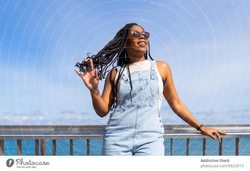 Fröhlicher Sommertag mit Freunden in Barcelona Frau MEER Glück jung Sonnenbrille Jeansstoff Latzhose Lächeln Freude lässig Mode Frisur Afroamerikaner Geflecht