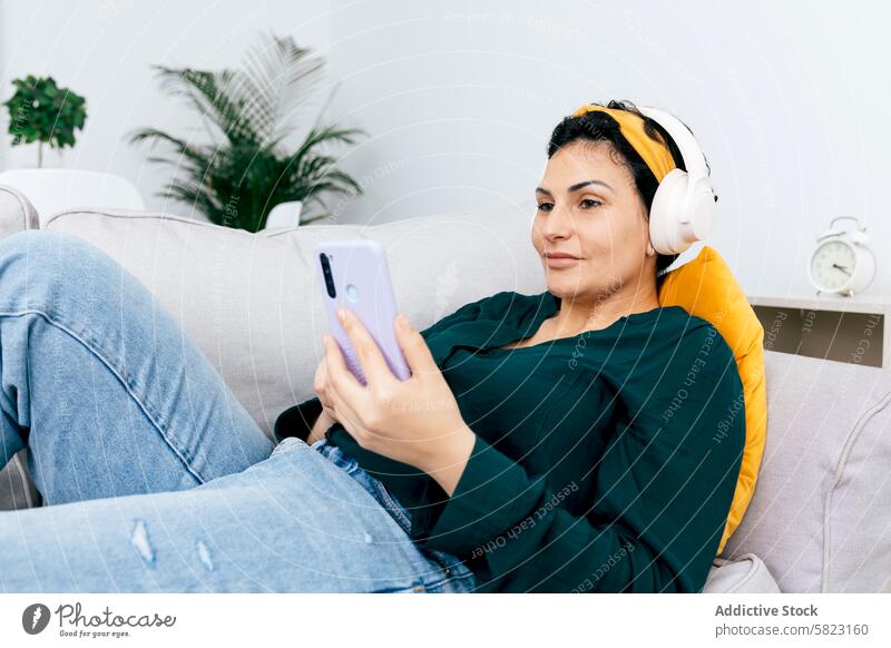 Frau, die zu Hause Musik hört und auf ihrem Smartphone surft Kopfhörer Sofa heimwärts Freizeit Browsen entspannt gemütlich Technik & Technologie Konnektivität