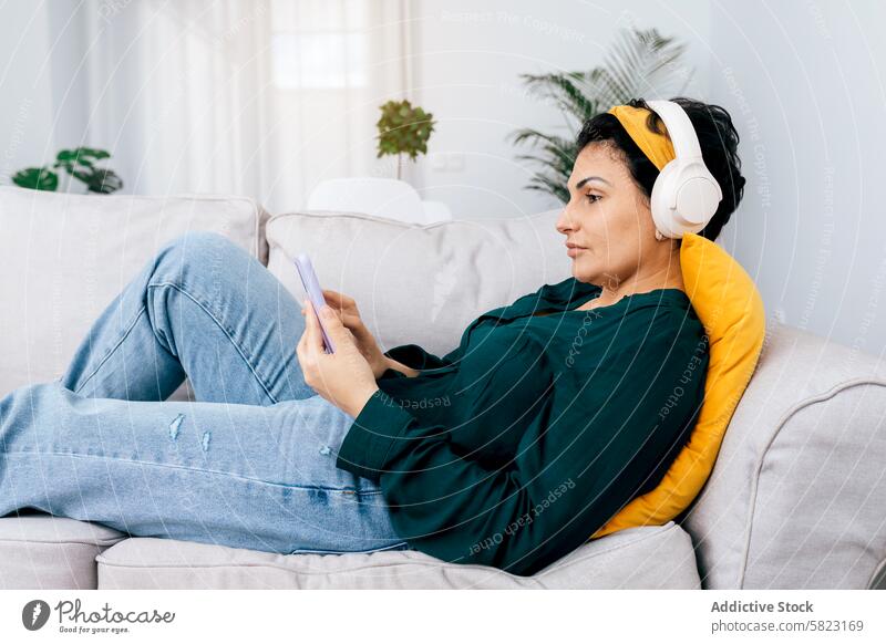 Frau entspannt auf Couch mit Smartphone und Kopfhörern Liege entspannend Freizeit heimwärts Musik Browsen Komfort lässig gemütlich im Innenbereich hören