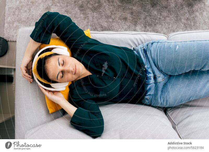 Junge Frau entspannt auf einer Couch mit Kopfhörern Musik entspannend Liege im Innenbereich lässig friedlich Inhalt gemütlich Freizeit Audio Genuss Erholung