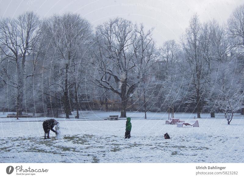 Park im Winter bei Schneefall. Erwachser und Kind bauen einen Schneemann Spiel Aktivität im Freien Spaß Kindheit spielen draussen Kälte Bewegung Eltern und Kind