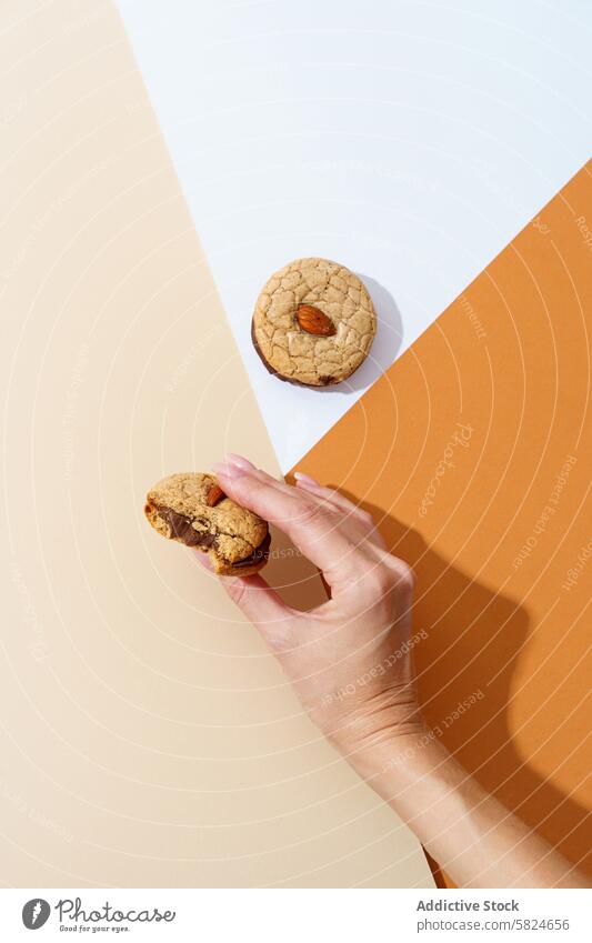 Hand, die einen Nusskeks auf einem zweifarbigen Hintergrund pflückt Biskuit Nut Kommissionierung selbstgemacht Keks Sahne orange Oberfläche Snack süß