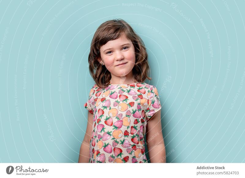 Junges Mädchen posiert in einem bunten Fruchtmuster Kleid Kind Lächeln türkis Hintergrund farbenfroh Muster bezaubernd heiter jung Mode Sommer niedlich Porträt