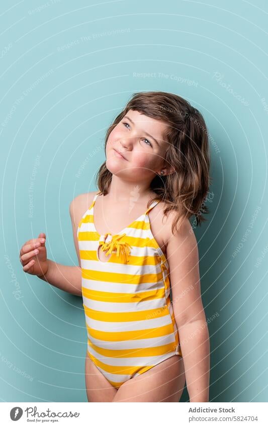 Junges Mädchen im gestreiften Badeanzug schaut nachdenklich auf Kind Sommer gelb weiß türkisfarbener Hintergrund jung aufschauend besinnlich Stehen niedlich