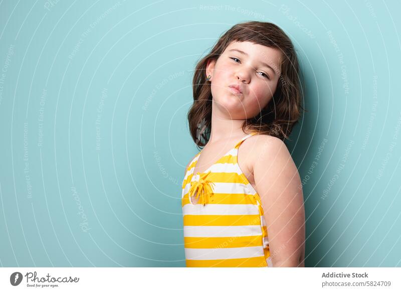Junges Mädchen posiert selbstbewusst in einem gestreiften gelben Badeanzug Pose spielerisch Kussmund gestreifte Badehose weiß blassblauer Hintergrund Fotokamera