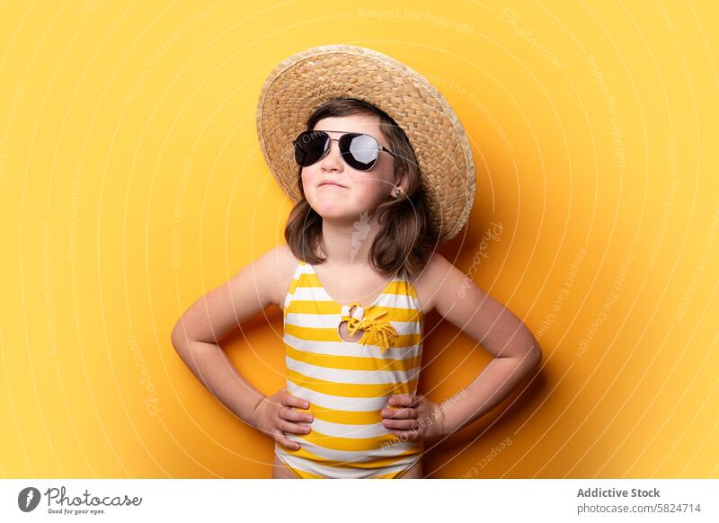 Junges Mädchen mit Strohhut und Sonnenbrille posiert selbstbewusst Selbstvertrauen gelber Hintergrund Streifen Badeanzug Mode Stil Kind Pose hell heiter Sommer
