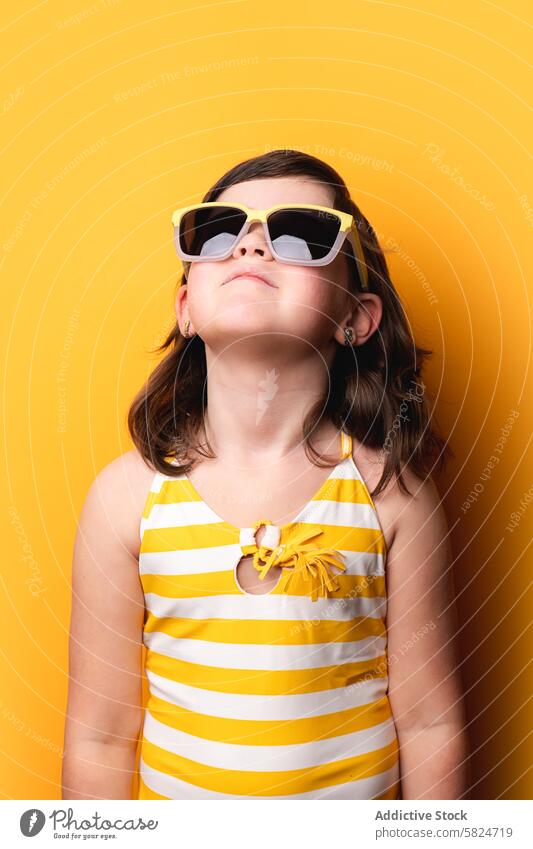 Junges Mädchen mit Sonnenbrille blickt auf gelbem Hintergrund gestreift Badeanzug heiter stylisch aufwärts Starrer Blick Mode Kind jung Farbe hell pulsierend