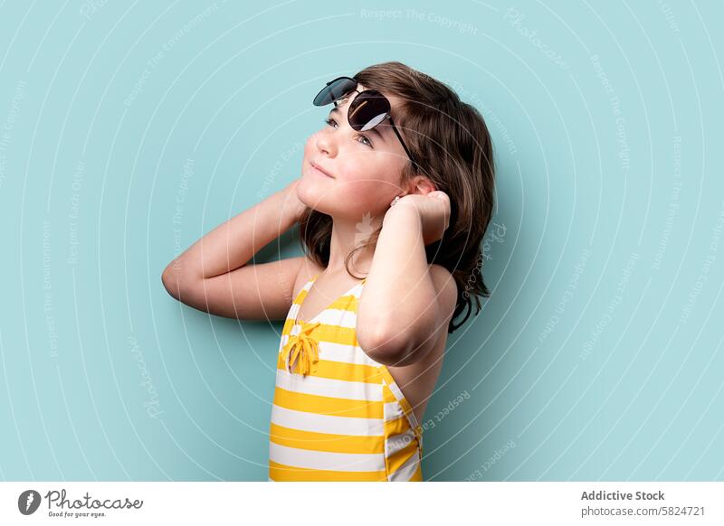 Junges Mädchen mit Sonnenbrille und Blick nach oben jung Kind brünett Badeanzug gestreift gelb weiß nachdenklich aufwärts Starrer Blick blaugrün Hintergrund
