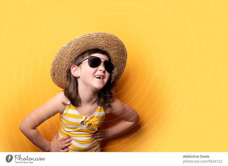 Junges Mädchen mit Strohhut und Sonnenbrille auf gelbem Hintergrund Sommer Hut spielerisch Lächeln Charme freudige Schwingung jung Kind heiter Mode Accessoire