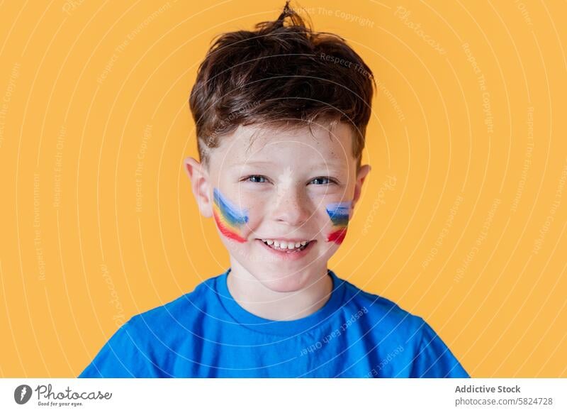 Junge mit buntem Gesicht malen auf einem gelben Hintergrund Lächeln Gesichtsfarbe Glück Kind blaues Hemd farbenfroh Malerei jung heiter Ausdruck Freude Spaß