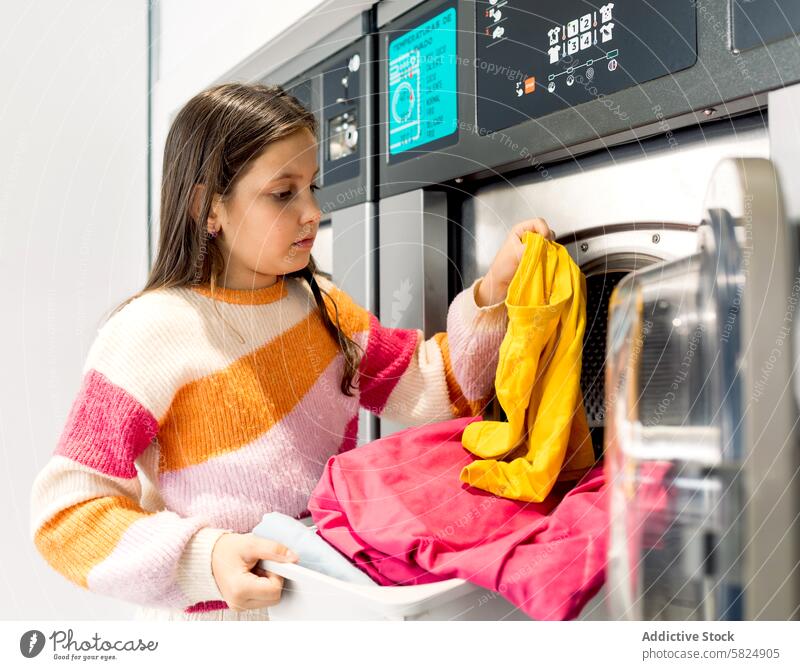 Mädchen im Teenageralter, das Wäsche wäscht und Kleidung inspiziert Kind Wäscherei Waschmaschine Bekleidung inspizierend Hausarbeit Wegsehen gelb rosa Pullover