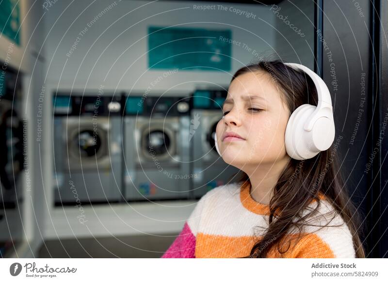 Preteen Mädchen entspannt sich mit Kopfhörern in einer Wäscherei Kind entspannend Musik Augen geschlossen tragend genießend Hintergrund Waschmaschinen