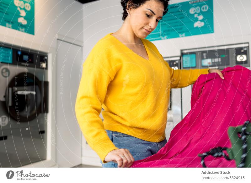 Frau sortiert Wäsche in einem öffentlichen Waschsalon Erwachsener Wäscherei Sortierung Kleidung Waschmaschine im Innenbereich Öffentlich rosa Schot hell