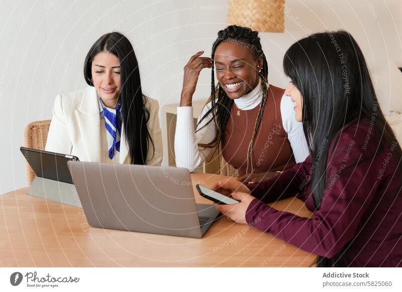 Drei unterschiedliche Frauen, die zu Hause an einem Laptop zusammenarbeiten heimwärts Zusammenarbeit Vielfalt Tisch im Innenbereich Besprechung freudig Teamwork