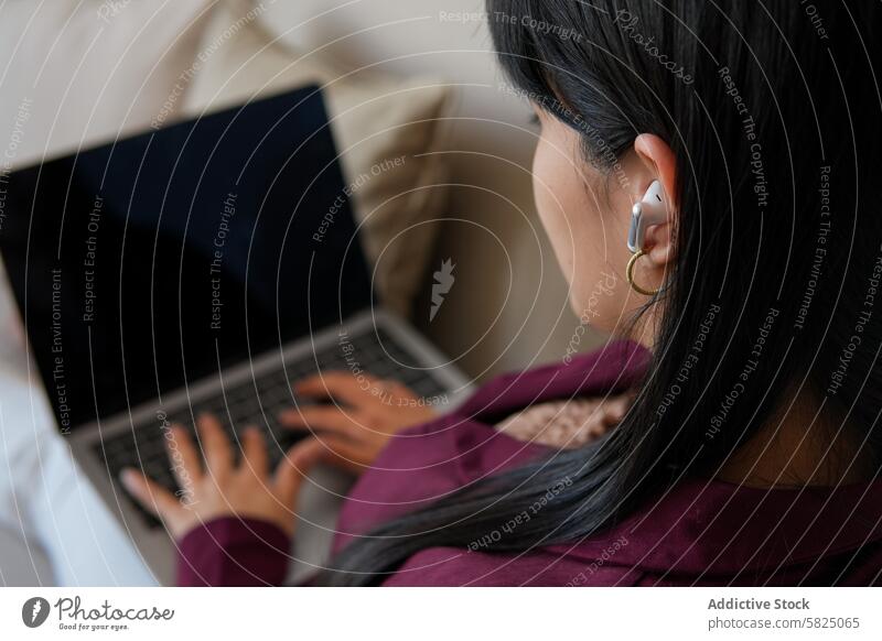 Junge Frau, die zu Hause am Laptop arbeitet heimwärts Fernarbeit Sitzen Technik & Technologie Ohrstöpsel Tippen Komfort freiberuflich Arbeit von zu Hause aus