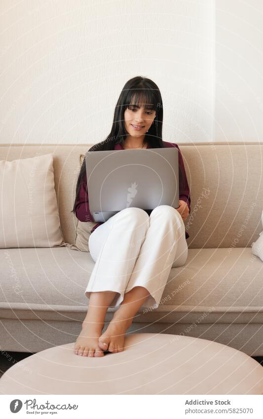 Frau arbeitet bequem von ihrer Couch aus zu Hause heimwärts Laptop Arbeit Liege lässig fokussiert im Innenbereich jung Büro abgelegen Arbeit von zu Hause aus