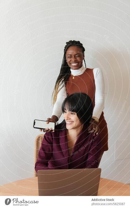 Zwei unterschiedliche Frauen, die zu Hause arbeiten und zusammenarbeiten heimwärts Arbeit Laptop Zusammenarbeit Freundschaft Freude vielfältig sitzend Stehen