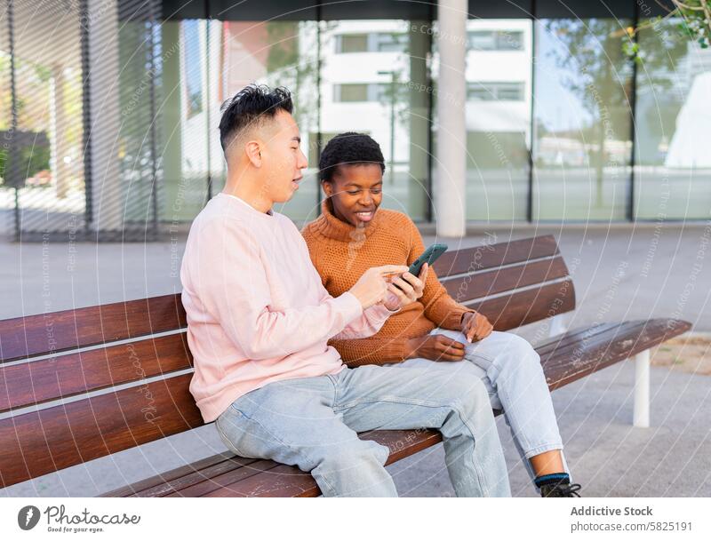 Zwei Freunde teilen einen Moment mit einem Smartphone auf einer Bank Freundschaft im Freien asiatischer Mann Afroamerikaner Technik & Technologie Anschluss