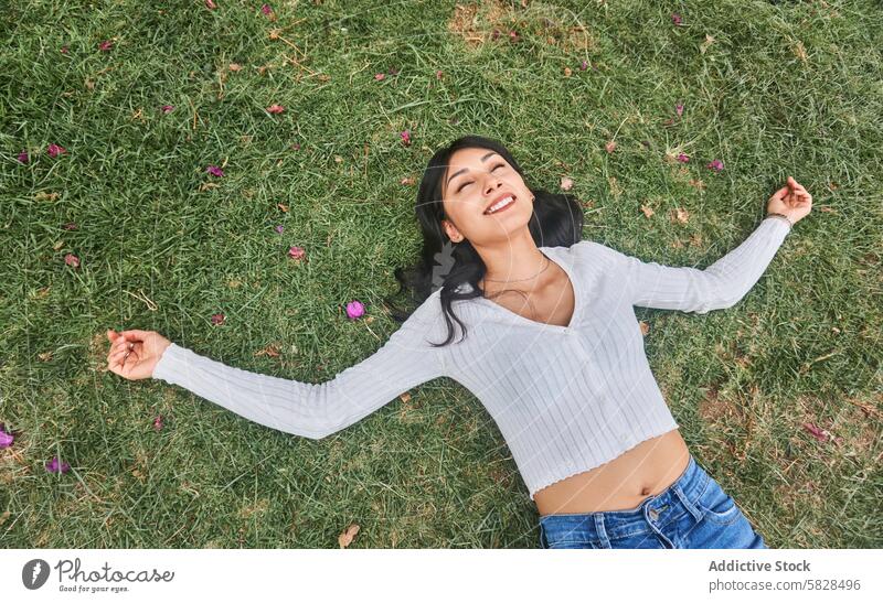 Junge Frau genießt einen entspannenden Moment in der Natur Erholung Park Gras liegend Feld Blütenblätter rosa gestreut im Freien Freizeit Fröhlichkeit lässig