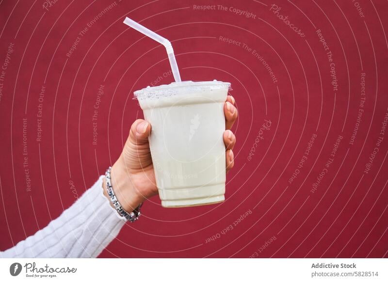 Hand hält einen Milchshake vor rotem Hintergrund Stroh trinken Nahaufnahme Getränk kalt Molkerei süß Leckerbissen Erfrischung Imbissbude Kunststoff schäumen