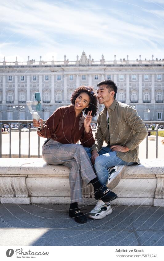 Lächelndes multiethnisches Paar macht ein Selfie vor dem Königspalast in Madrid Chinesisch hispanisch Spanien königlicher Palast Bank Sonnenschein Tourist