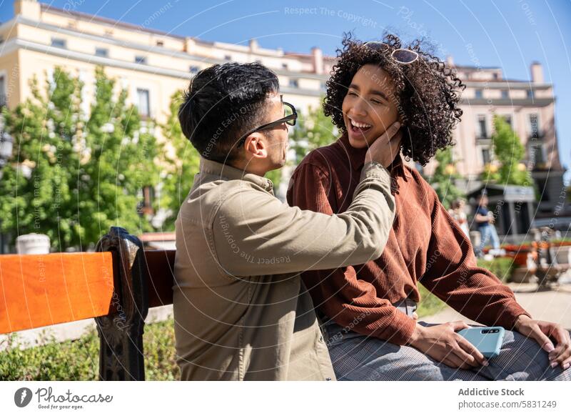 Ein multiethnisches Paar genießt einen sonnigen Tag zusammen in Madrid Chinesisch hispanisch Mann Frau Spanien Bank im Freien Park Lächeln Liebe Zuneigung