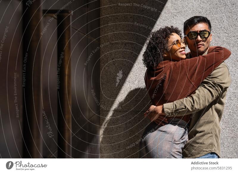 Ein multiethnisches Paar in einer zärtlichen Umarmung in den sonnigen Straßen Madrids Liebe Umarmen multikulturell Fröhlichkeit Spanien Vielfalt Sonnenbrille