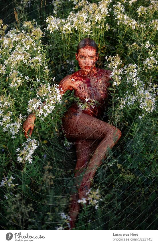 Diese grünen Felder mit weißen Blumen werden von einem nackten Mädchen besetzt, das mit Kunstblut bedeckt ist. Wie eine echte Satansanbeterin fühlt sie sich in ihrer nackten Haut pudelwohl. Eine hübsche Frau sieht aus wie ein Teufel.