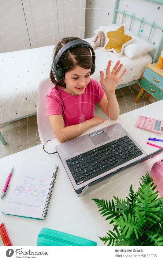 Junges Mädchen, das von zu Hause aus online lernt Kind Online-Lernen Bildung virtuelle Klasse Schlafzimmer Heimschule Laptop Kopfhörer winken heiter farbenfroh