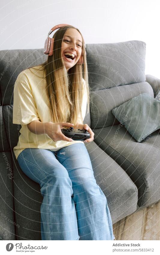 Fröhliche Frau spielt Videospiele auf der Couch zu Hause Spielen Glück Liege heimwärts Kopfhörer Regler Lächeln heiter Entertainment Freizeit jung Freude Spaß