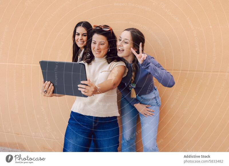 Frauen teilen einen Moment mit einem Tablet Tablette Interaktion Technik & Technologie Fröhlichkeit Freundschaft Lächeln digital orange Wand lässig Bekleidung