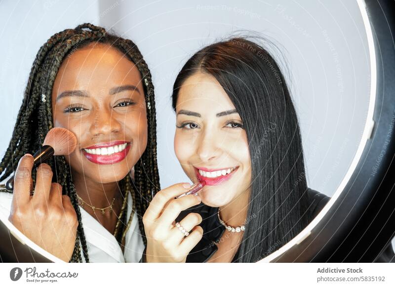 Zwei Frauen, die sich schminken und vor einem Ringlicht lächeln Make-up Lächeln Kosmetik Bürste Lippenstift Spiegel Schönheit Porträt vielfältig Freundschaft