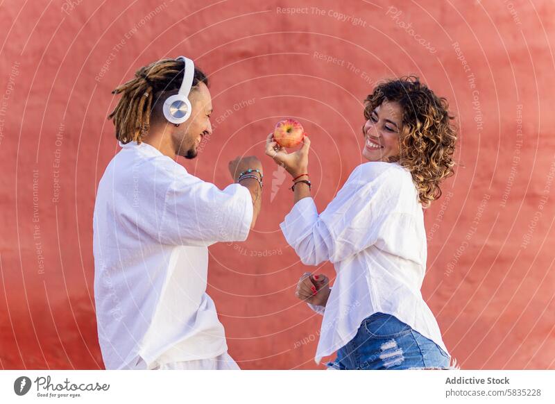 Zwei fröhliche Menschen, die im Freien einen Apfel austauschen Mann Frau Freude spielerisch Lächeln lässig weiß Top rot Wand Frucht Wechseln Teilen Freundschaft