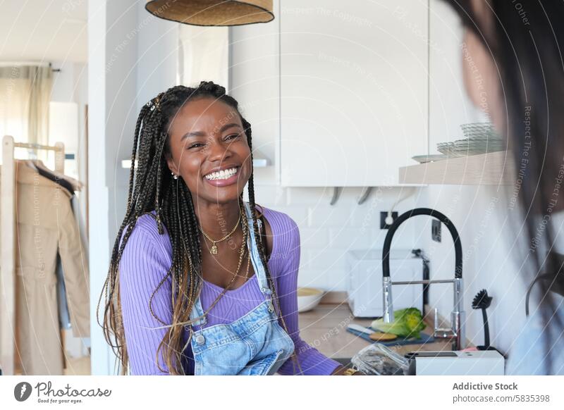 Junge Frau lacht in einer modernen Küche Lachen heiter hell geflochtenes Haar Jeansstoff Latzhose lavendelfarbenes Hemd Freude im Innenbereich Fröhlichkeit