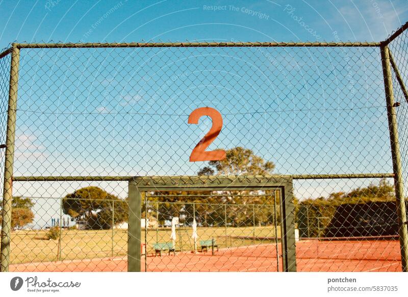 eine rostige 2 hängt über dem Eingang zu einem Tennisfeld. tennis tennisfeld tennisplatz zwei zahl nummerierung sportstätte abgrenzung Ballsport