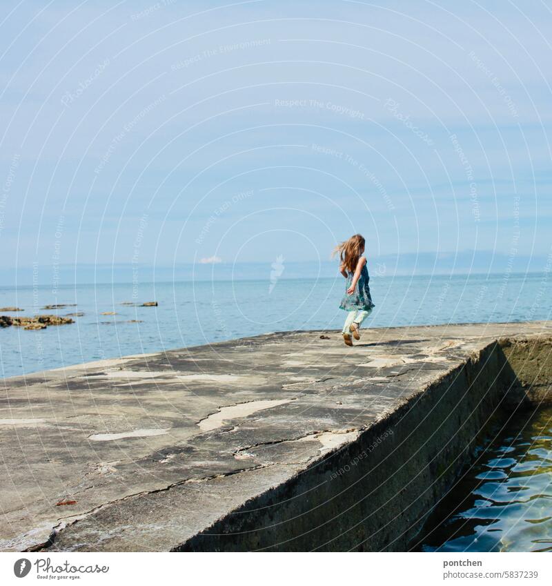 ein Kind läuft fröhlich und mit wehenden Haaren einen Steg  am Meer entlang. Glück meer urlaub steg ferien kleid Kindheit Fröhlichkeit Kaukasier Leben niedlich