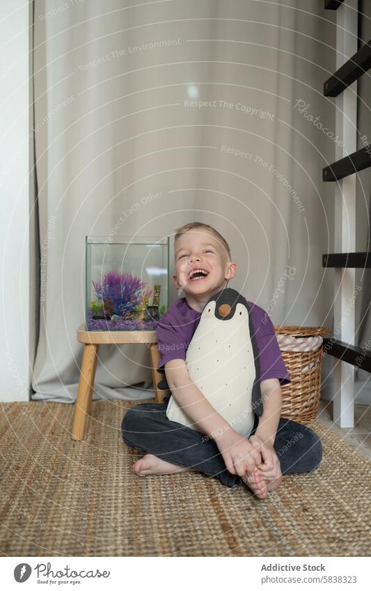 Junge mit Spielzeugpinguin erfreut sich zu Hause an Zierfischen Pinguin Haustier Fisch Tank heimwärts Lachen Freude Kind Tierpräparat Aquarium im Innenbereich