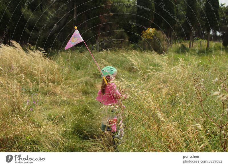 ein kind auf einem fahrrad mit wimpel im hohen gras kinderfahrrad mädchen rosa fahrradhelm ausflug fahrradtour gräser beschwerlich Fahrradfahren