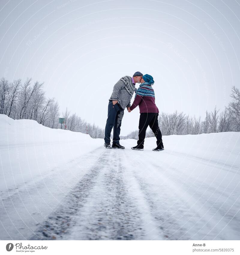 Ein älteres Paar in gestrickten isländischen Pullovern knutscht auf einer Straße in Finnisch-Lappland im Winter Küssen Isländerpullover kalt ältere Menschen