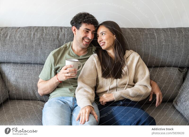 Glückliches Paar lächelnd und Kaffee genießend auf der Couch Sofa Lächeln heimwärts Interaktion Fröhlichkeit Sitzen jung bequem lässig warm im Innenbereich