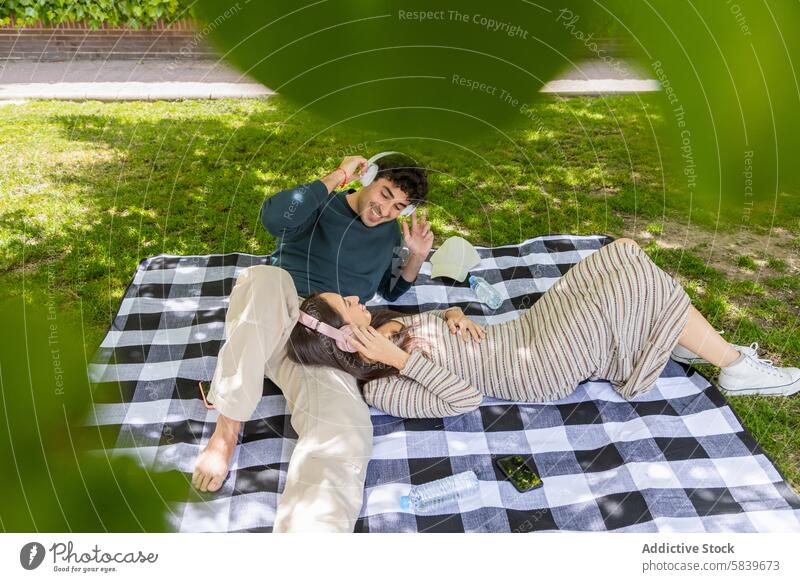 Pärchen genießt einen entspannten Moment auf einer Picknickdecke im Park Paar Decke Erholung Freude Kopfhörer Lächeln Frau Mann grün Schatten Freizeit im Freien