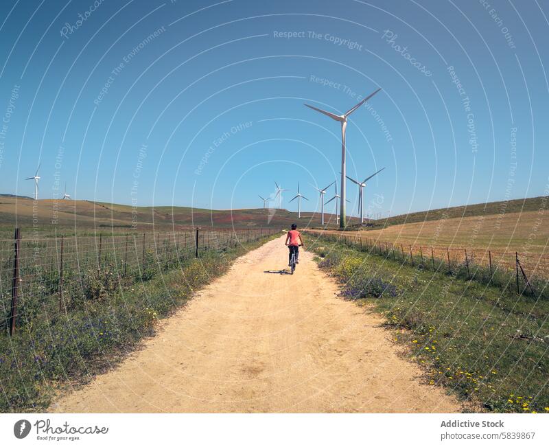 Unbekannter Radfahrer auf ländlichem Weg mit Windrädern in Cádiz Windkraftanlage Blauer Himmel Cadiz Mann Landschaft staubig reisen Energie regenerativ sonnig