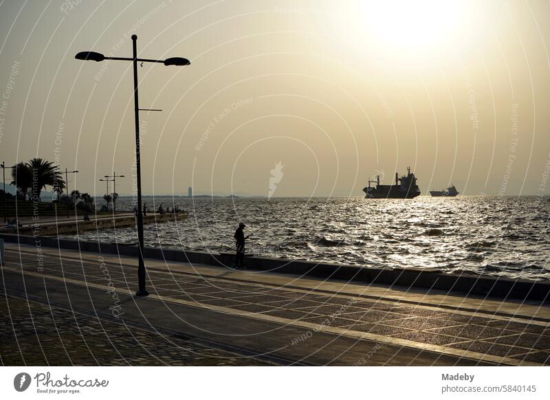 Blick von der Anlegestelle im Stadtteil Konak auf die Bucht von Izmir mit Anglern und ankernden Schiffen im Sommer vom Licht der Abendsonne am Ägäischen Meer in der Türkei