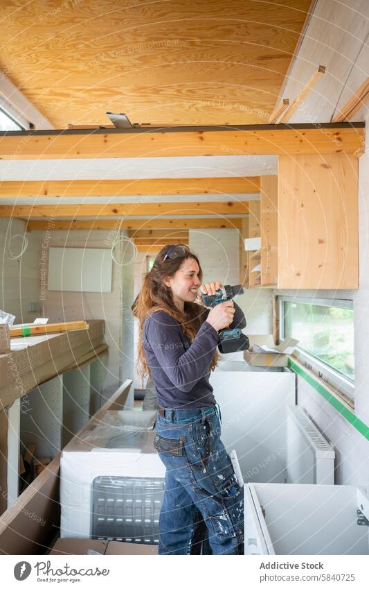 Junge Frau bei Heimwerkerarbeiten in einer hellen Werkstatt diy Arbeit Konstruktion bohren Schnurlos Werkzeug Lächeln sonnenbeschienen hölzern Schreinerei jung