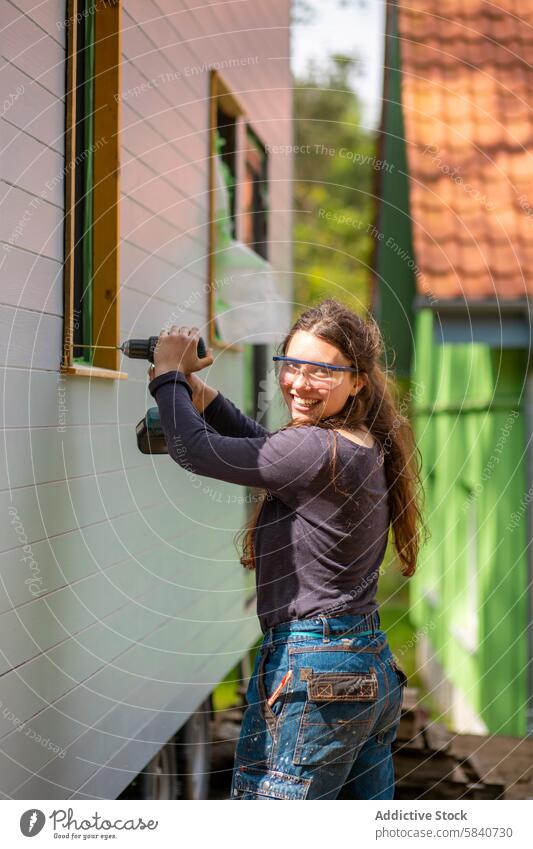 Junge Frau benutzt eine Bohrmaschine auf einem landwirtschaftlichen Gebäude im Freien jung diy Konstruktion Lächeln Bohrung Bauernhof sonnig Glück heiter Arbeit