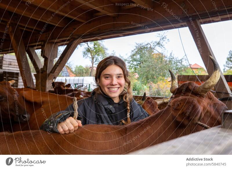 Lächelnde junge Frau genießt die Zeit mit den Rindern auf einem Bauernhof Scheune Landwirt rustikal idyllisch freudig Interaktion Herde braun Ackerbau