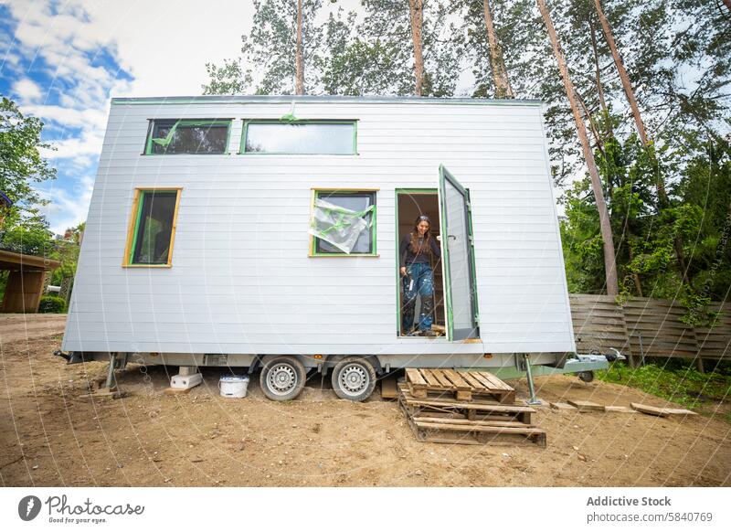 Junge Frau in einem kleinen Haus an einem sonnigen Tag jung kleines Haus Wagenräder ländlich kompakt lebend Tür Bäume modern nachhaltig Lifestyle Einfachheit