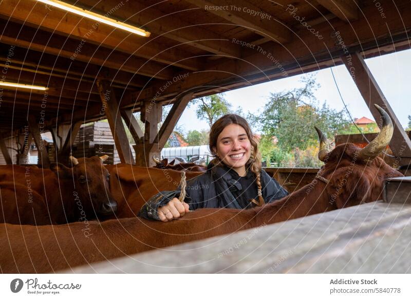 Junge Frau lächelt zwischen Rindern im Stall jung Lächeln Scheune Bauernhof rustikal Freude Landwirt Ackerbau Kuh Tier Viehbestand ländlich Glück Engagement