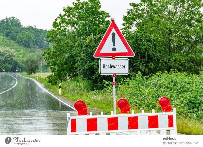 offizielle Straßenabsperrung wegen Hochwasser, mit Verkehrsschild,  vor regennasser Landstraße, im Hintergrund Weinberg, Bäume Regen rot-weiß grün
