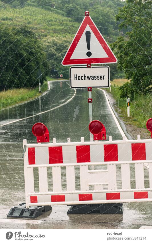 offizielle Straßenabsperrung wegen Hochwasser, mit Verkehrsschild,  vor regennasser Landstraße, im Hintergrund Weinberg, Bäume Regen Straßenschild Gefahr